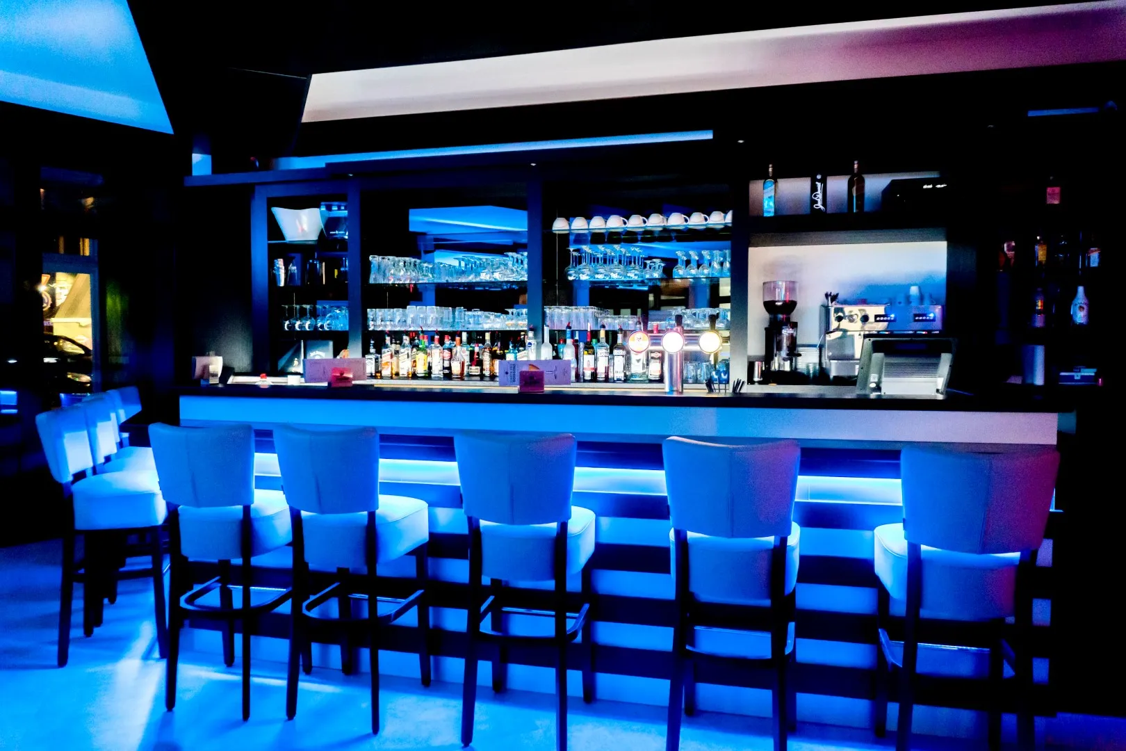 Le comptoir du Metropole éclairé en bleu, ses tabourets et ses étagères de verres