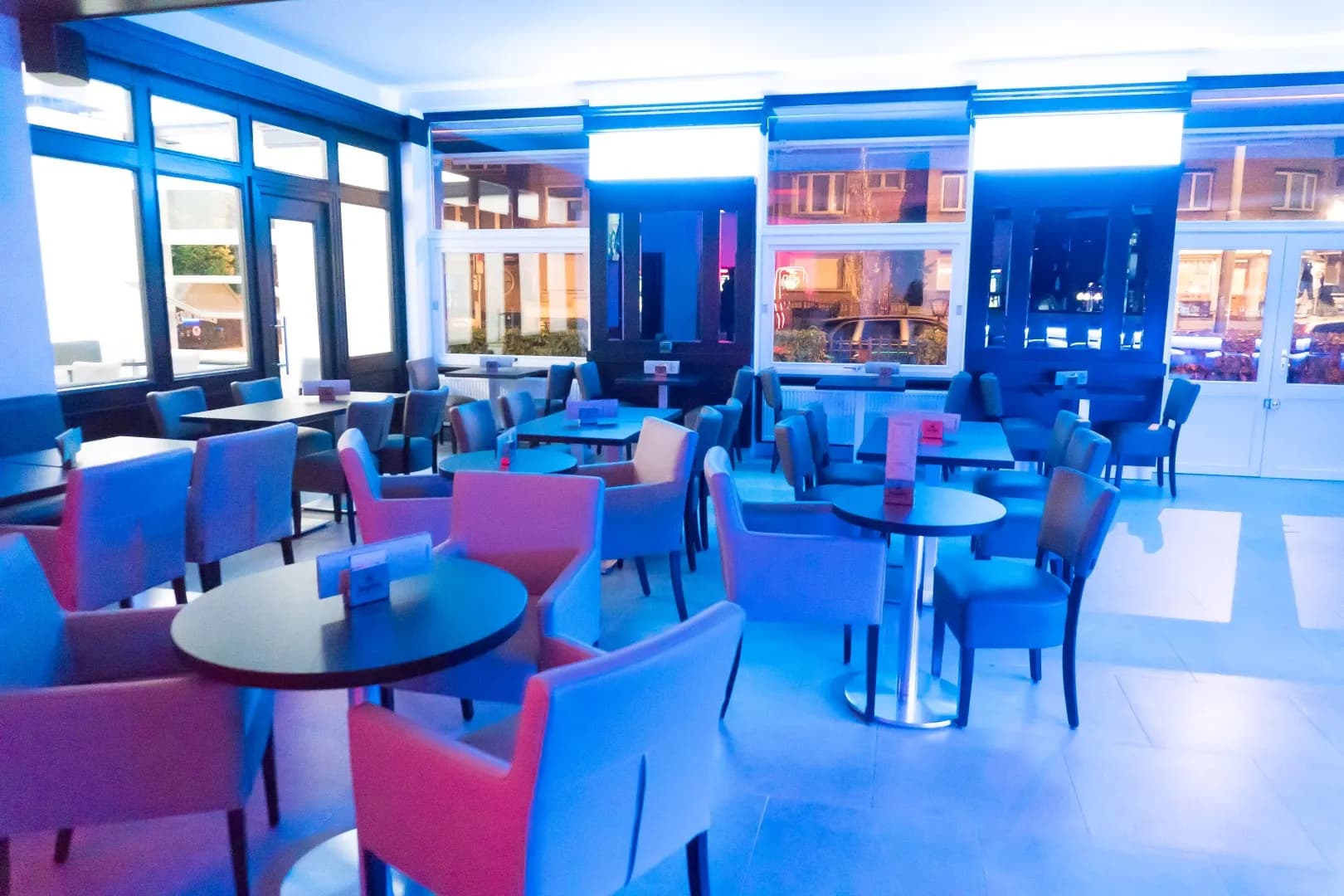 Les tables et fauteuils devant les grandes baies vitrées, éclairés en bleu et rose