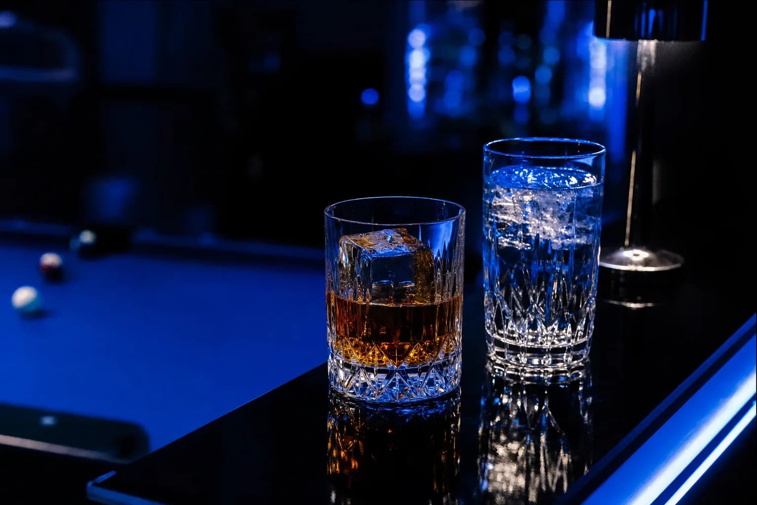 Un whisky sur glace et un gin tonic sur le comptoir, sous la lumière bleue